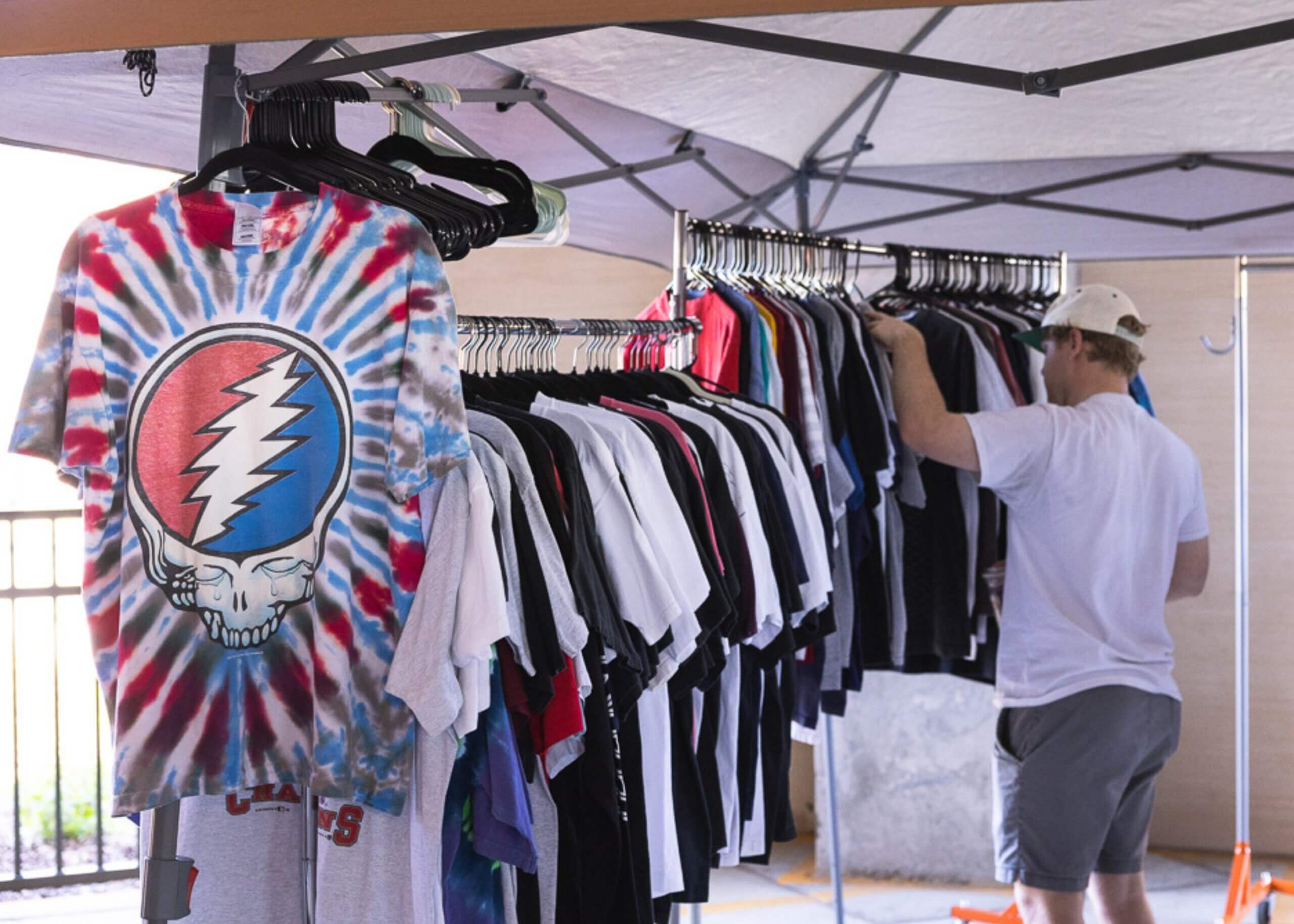 Photo of man thumbing through vintage t-shirts under outdoor tent